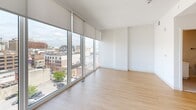 Located at 517 N Shipley Street in the heart of Wilmington, Delaware, this contemporary urban residence delivers a polished, modern aesthetic throughout its single-floor layout. Light wood-tone flooring runs continuously through the space, complementing the clean white walls and creating a bright, cohesive feel.

The living area is a standout, defined by expansive floor-to-ceiling windows that wrap around the corner, flooding the room with natural light and offering sweeping views of the Wilmington skyline and surrounding cityscape. Roller shades provide flexible light control without compromising the dramatic outlook.

The kitchen is thoughtfully designed with sleek flat-front white cabinetry extending to the ceiling, offering generous storage. A marble-inspired backsplash, matte black fixtures, and a full suite of stainless steel appliances — including a refrigerator, electric range, over-the-range microwave, and dishwasher — round out the functional and stylish space. Track lighting overhead adds a modern industrial accent.

The bathroom features neutral tile flooring, a white vanity with a framed mirror, and matte black hardware accents that echo the design language found throughout the unit.

An entry hallway with a closet provides a clean transition into the main living areas, completing this well-appointed urban residence.