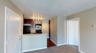 Located at 9505 Gold Coast in San Diego, this upstairs unit offers a well-appointed single-floor layout designed for comfortable everyday living. The open-concept kitchen is a central highlight, featuring rich dark wood cabinetry, granite-look countertops with a breakfast bar peninsula, and black appliances including a refrigerator, range, and over-the-range microwave. Track lighting above the kitchen provides focused illumination, enhancing the warmth of the cabinetry. The kitchen flows seamlessly into the living area, which is finished with plush carpeting that adds a cozy, residential feel. Rich hardwood flooring transitions the space between the kitchen and living areas, creating a natural visual distinction between zones. Neutral-toned walls throughout contribute to a bright and airy ambiance, complementing the overall clean aesthetic. A tall storage unit provides additional organizational space, while a paneled door leads to further rooms within the unit. The layout is efficient and thoughtfully arranged, making good use of the available space while maintaining an open, uncluttered feel. This unit at Gold Coast presents a practical and inviting living environment in a convenient San Diego location.