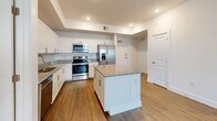 Located at 1414 SW 17th Pl in Cape Coral, Florida, this single-story home offers a clean, modern design with consistent wood-look flooring and a bright, neutral color palette throughout. The kitchen serves as a standout feature, showcasing white shaker-style cabinetry, granite countertops, a full suite of stainless steel appliances including a range, microwave, dishwasher, and French door refrigerator, and a central island with additional counter space. Recessed lighting and a tray ceiling detail add architectural interest to this well-appointed space. The living areas are generously sized, with high ceilings in select rooms, ceiling fans, and windows dressed with blinds that allow for natural light. Each bedroom provides a comfortable, open layout with ample room for furnishings. The bathroom features a glass-enclosed walk-in shower with white subway tile walls and chrome fixtures, delivering a clean and functional design. Storage is well considered, with walk-in closets fitted with wire shelving systems. A dedicated laundry area houses a full-size washer and dryer alongside additional shelving. The open floor plan connects living, dining, and kitchen spaces seamlessly, creating a cohesive and practical layout suited to everyday living.