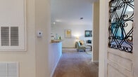 Located at Floral Springs Blvd in Port Orange, Florida, this single-story residence offers a well-designed, open-concept layout that balances functionality with a warm, inviting ambiance. Neutral tones, plush carpeting throughout the living areas, and tile flooring in the kitchen and bathrooms create a cohesive interior palette.

The kitchen is thoughtfully laid out in a galley style, featuring warm wood cabinetry, black appliances including a range and refrigerator, a built-in dishwasher, and light tile flooring. A breakfast bar connects the kitchen to the adjacent dining area, which is defined by a teal accent wall and receives overhead lighting, creating a distinct yet open dining space.

The living room is bright and comfortable, with natural light filtering through large windows dressed with decorative curtains. The bedrooms are carpeted and well-proportioned, each offering natural light through windows and ample space for furnishings. One bedroom includes a ceiling fan, while another features softer, warmer lighting suited for a primary suite.

The bathroom presents a clean, functional design with a wide vanity, a large mirror, tile flooring, and a shower enclosure. Throughout the residence, the consistent use of warm neutral walls and soft lighting contributes to a relaxed, comfortable atmosphere.