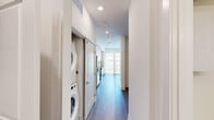 Located at 2950 Brighton Blvd in Denver's vibrant River North Art District, this efficiently designed single-floor unit offers a thoughtfully organized layout across a compact footprint. The open kitchen is a standout feature, showcasing floor-to-ceiling white cabinetry, dark granite countertops, a stone mosaic tile backsplash, and a full suite of stainless steel appliances including a refrigerator, range, microwave, and dishwasher. Recessed lighting and wood-look flooring carry throughout the space, lending warmth and continuity. The hallway serves as a practical connector, housing a stacked washer and dryer unit conveniently tucked alongside closet access. A large sliding glass door in the living area invites an abundance of natural light and frames views of the surrounding Denver skyline and neighboring architecture. The bathroom is finished with large-format marble-style tile flooring and wall surrounds, a glass-enclosed walk-in shower with elegant brushed gold hardware, and a built-in storage cabinet, creating a clean and refined aesthetic. The overall ambiance is modern and minimalist, with a bright, neutral palette that maximizes the sense of space throughout.