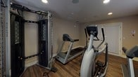 This single-level fitness center offers a practical and fully equipped space designed to support a well-rounded workout routine. The room features durable wood-style flooring that provides a clean, modern aesthetic while standing up to the demands of daily exercise use. Neutral-toned walls and white baseboards give the space a tidy, professional appearance throughout.

The fitness center is outfitted with Matrix-brand commercial-grade equipment, including multiple treadmills, an elliptical machine, and a multi-function cable strength training unit, providing options for both cardiovascular and resistance training. Recessed ceiling lights ensure the space is well-lit, while ceiling-mounted vents provide climate control for comfort during workouts.

A corner shelf holds a television set, allowing users to watch programming during their session. A freestanding water cooler is conveniently positioned nearby, keeping hydration accessible at all times. A small waste bin is also present for added convenience.

Windows fitted with horizontal blinds allow natural light to filter into the room while maintaining privacy. Informational signage, including fitness center rules, is posted on the walls. The space is single-floor and accessed through a door with louvered blinds. Overall, the fitness center delivers a functional and comfortable environment suited for everyday exercise needs.