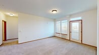 Located at 5101 S Freya St in Spokane, WA, this one-bedroom, one-bathroom unit offers a practical and comfortable layout across a single floor. The open-concept living area is generously sized, featuring soft wall-to-wall carpeting, neutral white walls, and warm wood baseboards that run throughout. Large windows and a glass door leading to a private balcony flood the space with natural light and offer pleasant outdoor views of the surrounding landscape.

The kitchen is equipped with warm honey-toned cabinetry, a tile backsplash, and a full suite of white appliances including a refrigerator, stove, and microwave. A peninsula counter with an extended breakfast bar separates the kitchen from the living area, making it ideal for both cooking and casual dining. Hardwood-style flooring adds warmth to the kitchen and entryway.

The spacious bedroom features carpeted floors, a bright window with outdoor views, and a dedicated walk-in closet outfitted with multi-tier wire shelving for ample storage. The bathroom includes a wide vanity with wooden cabinetry, a well-lit mirror, a tiled floor, and a full bathtub with shower. Baseboard heating and a wall-mounted A/C unit ensure year-round comfort throughout the unit.