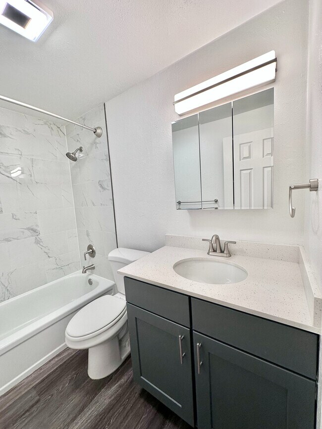 Elegante baño con accesorios modernos, que incluye ducha con azulejos de mármol, tocador con espejo y elegante suelo de madera. - Lamar Station