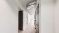 This thoughtfully designed two-bedroom, three-bathroom residence in Royal Oak, Michigan offers a modern aesthetic across a comfortable single-floor layout. The interior is defined by light hardwood-style flooring, crisp white walls, and bold dark-finished doors that create a striking contrast throughout. The hallway makes an architectural statement with exposed metallic ductwork running overhead, adding an industrial-chic character to the otherwise clean, contemporary design. The kitchen is a standout feature, showcasing high-gloss white upper cabinetry paired with warm wood-toned lower cabinets, quartz countertops, a subway tile backsplash, and a full suite of stainless steel appliances. The primary bedroom is generously sized and is served by a well-appointed en-suite bathroom featuring a double-sink vanity with warm wood cabinetry, a backlit mirror, large-format tile flooring, and a glass-enclosed walk-in shower. A dedicated walk-in closet with built-in shelving and hanging rods provides excellent storage. The secondary bedroom includes a ceiling fan and a double-door closet. All bathrooms maintain a consistent, modern finish palette. A dedicated laundry room houses a full-size washer and dryer with overhead wood-cabinet storage, adding everyday convenience to this polished Royal Oak residence.