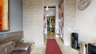 Located at 434 SW College St in Portland, Oregon, this single-floor lobby and hallway space offers a striking industrial-chic aesthetic that blends raw materials with curated design details. Polished concrete floors stretch throughout, complemented by exposed concrete block walls and structural columns that reinforce the building's urban character. A dramatic reclaimed wood accent wall anchors the entry lounge area, where modern swivel chairs and a glass side table create a welcoming seating nook beneath pendant lighting. A vibrant cherry blossom mural — painted in bold reds against a neutral backdrop — serves as a standout artistic centerpiece, adding warmth and visual energy to the space. Large glass entry doors at the front invite natural light into the lobby, offering views to the street beyond. The hallway corridor, lined with concrete masonry block walls and lit by simple pendant fixtures, guides visitors deeper into the building. A dedicated mailroom area features a full bank of individual tenant mailboxes alongside an elevator and stairwell access. Exposed ductwork overhead adds to the industrial character. Notably, the space includes a recreational nook housing classic arcade machines and a pinball table, reflecting a playful, community-oriented design approach. Bold artwork and a rich material palette make this lobby a memorable and functional gateway to the building.