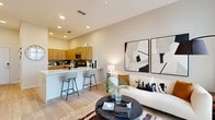 Located on International Drive in Orlando, FL, this well-appointed one-bedroom, one-bathroom residence offers a thoughtfully designed single-level layout. The open-concept kitchen and living area serves as the heart of the home, featuring light wood-tone cabinetry extending from floor to ceiling, white quartz countertops, a tiled backsplash in soft gray, and stainless steel appliances including a range, microwave, and dishwasher. A breakfast bar with seating connects the kitchen to the living space, creating an ideal flow for everyday living and entertaining. Light wood-style flooring runs throughout the main area, enhancing the bright, airy atmosphere complemented by recessed lighting and a ceiling fan. The living room is bathed in natural light through large windows and a glass door that opens to a private outdoor area. The spacious primary bedroom features plush carpeting, large windows with sheer drapes, and ample room for a full furniture arrangement. The bathroom is finished with wood-tone cabinetry, white countertops, wood-look tile flooring, and a tub/shower combination with clean white subway tile surround. Throughout, the design maintains a cohesive modern aesthetic with neutral tones and quality finishes.