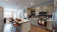 This thoughtfully designed single-floor residence combines contemporary finishes with bold, eclectic styling throughout. The open-concept kitchen serves as a central hub, featuring light wood-grain cabinetry, a classic brick-style tile backsplash, stainless steel appliances, and a spacious island with a white quartz countertop and seating — ideal for casual dining or entertaining. Warm wood-look flooring flows seamlessly through the main living areas, anchored by stylish pendant lighting overhead.

The living room makes an immediate impression with a dramatic teal accent wall, large windows, and a private exterior door that invites natural light deep into the space. The primary bedroom is bright and welcoming, with oversized windows and access to an ensuite bathroom complete with a glass-enclosed shower, dual vanity with quartz countertops, and a spacious walk-in closet with custom shelving. A second bedroom offers a comfortable, well-proportioned layout, while a second full bathroom features a clean, modern vanity and tiled shower. An additional walk-in closet provides exceptional storage capacity. Throughout, the residence balances contemporary design with warm, livable character.