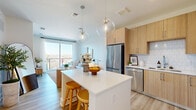 Located at 2490 N Druid Hills Rd in Atlanta, GA, this thoughtfully designed one-bedroom, two-bathroom residence offers a bright and modern living experience on a single floor. The open-concept layout seamlessly connects the kitchen and living room, creating an efficient and inviting communal space. The kitchen is outfitted with light wood cabinetry, white subway tile backsplash, stainless steel appliances, and a white quartz-topped island with bar seating, illuminated by globe pendant lights. Light wood-style flooring runs throughout, enhancing the airy feel. The living room is bathed in natural light from a large sliding glass door that opens to a private balcony, offering outdoor views of the Atlanta skyline and tree line. The bedroom features dual windows that flood the room with natural light and provide additional outdoor views, creating a calm and restful retreat. An in-unit stacked washer and dryer adds everyday convenience. Two well-appointed bathrooms include a walk-in glass-enclosed shower with white tile surround and wood-toned accents. Clean white walls, contemporary fixtures, and a neutral palette throughout lend the space a cohesive, modern aesthetic ideal for comfortable urban living.