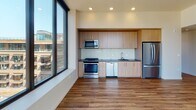 Located in Portland's vibrant Northwest District, this contemporary single-floor residence offers a thoughtfully designed layout filled with natural light. The open kitchen is a standout feature, showcasing light wood cabinetry, dark countertops, a subway tile backsplash, and a full suite of stainless steel appliances including a gas range, microwave, dishwasher, and refrigerator. Large floor-to-ceiling windows flood the living areas with sunlight while framing impressive views of the Portland skyline and surrounding hills. Warm hardwood-style flooring runs throughout, adding a cohesive and inviting feel to every room. The bedrooms are generously sized and benefit from oversized windows that continue the connection to the outdoors and city scenery. Two bathrooms serve the residence: one features a soaking tub with tiled surround and a lighted vanity mirror, while the other includes a glass-enclosed walk-in shower with elegant tile work. A stacked washer and dryer unit with overhead cabinetry is smartly integrated into the second bathroom, offering exceptional in-unit convenience. A well-proportioned hallway with recessed lighting and a built-in closet connects the private areas of the home. Clean neutral walls, recessed lighting throughout, and modern finishes come together to create a polished, move-in-ready space.