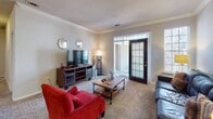 Located at 1400 Laurel Springs Dr in Durham, NC, this single-floor residence offers a well-organized layout designed for comfortable living. The living room serves as a central gathering space, featuring crown molding, a textured ceiling, carpet flooring, and a glass-paneled door that opens to an outdoor patio, allowing for an abundance of natural light. An adjacent sitting or sunroom area provides additional lounging space with large windows and its own patio door access. The dining area is defined by elegant crown molding, chair-rail wainscoting, and a pendant light fixture overhead, creating a refined atmosphere for meals. The kitchen is equipped with stainless steel appliances, including a refrigerator and electric range, complemented by white cabinetry and dark countertops. The bedrooms include a primary suite with carpet flooring, a ceiling fan, and a large window, as well as a secondary bedroom configured to accommodate twin beds. Bathrooms feature tub-shower combinations with white subway tile surrounds, dark countertop vanities with white cabinetry, and tile flooring. A dedicated in-unit laundry room with a full-size washer and dryer completes this functional and well-appointed home.