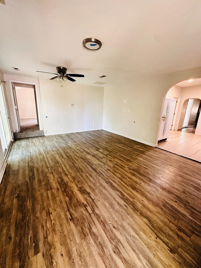 Acogedora sala de estar con elegantes pisos de madera, ventilador de techo y arco que conduce a una cocina luminosa. - 1385 Yukon Street