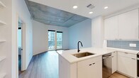 Located at 1801 Patterson Street in Nashville's vibrant 37203 corridor, this modern one-bedroom, one-bathroom residence offers a thoughtfully designed open-concept layout. Light hardwood flooring flows throughout, complemented by crisp white walls and recessed lighting that create a bright, contemporary atmosphere.

The kitchen is a standout feature, outfitted with sleek flat-front white cabinetry extending to the ceiling, a blue-gray subway tile backsplash, and a full suite of stainless steel appliances including a refrigerator with ice maker, range, microwave, and dishwasher. A peninsula with a white quartz countertop and undermount sink provides additional workspace and seating potential while opening seamlessly to the combined dining and living area. A distinctive exposed concrete coffered ceiling adds an industrial-chic design element to the main living space, which leads to a private balcony with outdoor views.

The well-proportioned bedroom features the same exposed concrete ceiling detail and a ceiling fan, while three closets — including a carpeted walk-in — provide generous storage. The bathroom includes a glass-enclosed walk-in shower with white subway tile and warm wood-tone flooring. A dedicated laundry area and in-unit storage round out this efficiently planned Nashville residence.