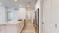This well-designed one-bedroom, one-bathroom unit offers a thoughtfully organized single-floor layout that maximizes functionality. The open-concept kitchen and living area serves as the heart of the unit, featuring light wood-style flooring throughout. The kitchen is equipped with stainless steel appliances, including a French door refrigerator, electric range, and microwave. A peninsula island with a granite countertop and undermount sink provides both prep space and a casual dining option. White shaker-style cabinetry with sleek hardware and a subtle tile backsplash complete the kitchen's clean, modern aesthetic.

The living area benefits from recessed lighting, a ceiling fan, and a glass-paneled door that welcomes natural light. The bedroom is carpeted for comfort, features two windows for additional natural light, a ceiling fan, and direct access to a dedicated closet and the bathroom. The bathroom includes a tiled tub-shower combination and wood-style flooring that ties into the rest of the unit. A hallway connects the bedroom and bathroom, maintaining a logical and private flow. Throughout, crisp white walls and neutral tones create a bright, cohesive atmosphere.