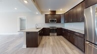 This single-floor residence combines contemporary design with high-quality finishes throughout. The open-concept living area is finished with light-toned luxury vinyl plank flooring and neutral walls, creating a bright, versatile space. A ceiling fan adds comfort, while a door leads to a private outdoor area with views of surrounding trees, allowing natural light to filter in.

The kitchen is a standout feature, equipped with rich dark-espresso cabinetry, marble-look countertops, a herringbone tile backsplash, stainless steel appliances, and a peninsula with an undermount sink — ideal for both cooking and entertaining. The layout flows seamlessly into the living and dining areas.

A dedicated den or home office provides a functional retreat, featuring wood-look flooring consistent with the rest of the unit. A separate laundry room with full-size washer and dryer adds everyday convenience.

The bathroom showcases floor-to-ceiling marble-look tile in the walk-in shower, a dark-cabinetry vanity with marble countertops, and a well-lit mirror. A private water closet with marble-look tile flooring is accessible nearby. The overall design palette is cohesive, clean, and modern throughout.