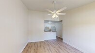 Located at 7800 SE Woodview Terr in Hobe Sound, FL, this efficient one-bedroom, one-bathroom residence offers a clean, updated interior across a single floor. Light wood-look flooring runs throughout the unit, creating a cohesive and bright aesthetic. The open living area is anchored by a ceiling fan with light fixture and flows seamlessly into the kitchen via a half-wall pass-through. The kitchen features white shaker-style cabinetry, granite-patterned countertops, a white electric range, and a full-size refrigerator — all arranged in a functional layout. A dedicated laundry area adds everyday convenience. The bedroom is a comfortable size, fitted with its own ceiling fan, a window with blinds that allows natural light and views of the surrounding greenery, and a closet for storage. A hallway connects the main living spaces to the full bathroom, which includes a tub-shower combination with a handheld showerhead, toilet, and an overhead wall cabinet for storage. A wall-mounted HVAC unit and multiple windows support climate control and ventilation. The unit's neutral color palette and updated finishes give it a clean, move-in-ready feel suited for comfortable Florida living.