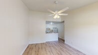 Located at 7800 SE Woodview Terr in Hobe Sound, FL, this efficient one-bedroom, one-bathroom residence offers a clean, updated interior across a single floor. Light wood-look flooring runs throughout the unit, creating a cohesive and bright aesthetic. The open living area is anchored by a ceiling fan with light fixture and flows seamlessly into the kitchen via a half-wall pass-through. The kitchen features white shaker-style cabinetry, granite-patterned countertops, a white electric range, and a full-size refrigerator — all arranged in a functional layout. A dedicated laundry area adds everyday convenience. The bedroom is a comfortable size, fitted with its own ceiling fan, a window with blinds that allows natural light and views of the surrounding greenery, and a closet for storage. A hallway connects the main living spaces to the full bathroom, which includes a tub-shower combination with a handheld showerhead, toilet, and an overhead wall cabinet for storage. A wall-mounted HVAC unit and multiple windows support climate control and ventilation. The unit's neutral color palette and updated finishes give it a clean, move-in-ready feel suited for comfortable Florida living.