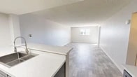 This well-appointed 2-bedroom, 1-bathroom residence in Albuquerque, New Mexico offers a clean, modern aesthetic across a single thoughtfully laid-out floor. The open living area is bright and airy, featuring light-toned wood-look flooring, neutral gray walls, a textured ceiling, and a window with outdoor views that allows natural light to fill the space. A sliding glass door provides additional light and outdoor access.

The kitchen is a functional standout, equipped with stainless steel appliances including an electric range, over-the-range microwave, and refrigerator. Two-tone cabinetry — white uppers and gray lowers — is paired with crisp white countertops and a classic subway tile backsplash. A double-basin stainless steel sink with a modern pull-down faucet completes the space.

Both bedrooms are carpeted in neutral tones and offer a comfortable, quiet retreat. The primary bedroom includes a sliding door to an outdoor area and direct access to a walk-in closet with dual hanging rods and built-in shelving. The second bedroom features textured walls and plush carpet.

The bathroom is finished with tile flooring, a tub-shower combo, white tile surround, and a vanity with stone-look countertops. A hallway connects the rooms, adding to the unit's organized flow.