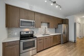 Located at 4440 Twain Ave, Unit 215 in San Diego, California, this single-floor residence offers a thoughtfully designed layout with modern finishes throughout. The kitchen is a standout feature, showcasing rich medium-toned wood cabinetry that extends to the ceiling, a full suite of stainless steel appliances including a refrigerator with ice maker, electric range, built-in microwave, and dishwasher. Light quartz countertops complement the textured tile backsplash, while a gooseneck faucet serves the undermount sink. Track lighting overhead provides ample task illumination, and a large window allows natural light to pour into the adjacent living area. The living space is finished with light wood-look flooring that carries throughout the unit, contributing to a bright and cohesive aesthetic. The bedroom features the same warm flooring, a ceiling fan with integrated lighting, and access to a hallway with closet space. The bathroom is finished with crisp white square wall tiles and includes a soaking tub and shower combination with brushed gold fixtures, offering a clean and contemporary feel. Overall, the unit presents a modern, well-maintained living environment suited for comfortable everyday living in San Diego.
