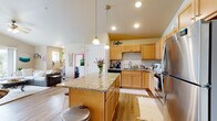 Located at 816 Brewster Dr in Lake Mills, Wisconsin, this single-floor home presents an open-concept design characterized by vaulted ceilings that lend a sense of spaciousness throughout the main living areas. Light wood-tone flooring flows through the kitchen and living room, enhancing the bright, airy atmosphere created by natural light from multiple windows and sliding glass doors.

The kitchen is a functional centerpiece, featuring warm maple cabinetry extending to the ceiling, granite countertops, a suite of stainless steel appliances including a refrigerator, range, and microwave, and a generously sized island with seating for several. Pendant lighting above the island adds a polished touch. The kitchen opens seamlessly into the living area, which benefits from vaulted ceilings, a ceiling fan, and a sliding glass door offering outdoor views and access to a balcony or patio.

The primary bedroom features vaulted ceilings, plush carpeting, a ceiling fan, a walk-in closet, and a sliding glass door leading to a private outdoor space. A full bathroom is finished with granite countertops and warm cabinetry. Throughout, the home maintains a cohesive, welcoming ambiance with neutral tones and an efficient, well-connected floor plan.