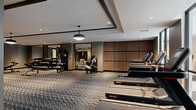 Located at 1991 Main Street in Sarasota, Florida, this professionally designed fitness center spans an impressive single floor, offering a comprehensive exercise environment suited for a wide range of training disciplines. The space is divided into distinct functional zones, each thoughtfully appointed to support a specific workout focus.

The main exercise floor is finished with a bold chevron-patterned carpet that adds visual sophistication while providing underfoot comfort during strength and conditioning workouts. This primary zone houses a robust selection of free weights, weight benches, cable machines, rowing ergometers, and multi-use strength equipment, all arranged to maximize usability and flow.

A dedicated cycling studio features light hardwood-style flooring and an expansive floor-to-ceiling mirror wall that visually extends the space and supports form monitoring during spin sessions. Adjacent areas accommodate cardio machines, including a row of Star Trac treadmills positioned along warm wood-paneled walls.

Throughout the facility, a series of stylish pendant lights complement recessed ceiling fixtures, casting bright, even illumination across every zone. Coffered ceiling detailing adds architectural refinement, while structural columns are integrated seamlessly into the layout. Large glass-panel partitions allow sightlines across zones, creating an open, connected feel throughout this expansive and well-equipped fitness facility.