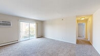 Located at 151 S Bishop Ave in Secane, PA, this two-bedroom, two-bathroom apartment offers a well-organized single-floor layout with approximately 900 square feet of living space. The open living area is finished with wall-to-wall carpet and neutral tones throughout, creating a bright and clean atmosphere. Sliding glass doors lead to a private balcony with views of the surrounding landscaped grounds and brick residential buildings. Baseboard heating and a wall-mounted air conditioning unit provide year-round climate control. The kitchen features rich oak cabinetry with raised panel doors on both upper and lower sections, light-toned countertops in an L-shaped configuration, and a stainless steel sink. Two well-sized bedrooms offer carpeted floors, natural light from windows with blinds, and generous closet space—including a dedicated walk-in closet with built-in shelving. The two full bathrooms include a tiled tub/shower combo with white square tile surround, while a second bathroom features wood-look flooring, a wall-mounted sink with chrome fixtures, and elegant sconce lighting with a mirrored medicine cabinet. A hallway connects all rooms, providing a functional and efficient floor plan throughout.