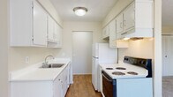 This single-floor residence offers a clean, functional layout designed for comfortable everyday living. The galley-style kitchen is efficiently organized with ample white cabinetry lining both walls, providing generous storage space. It features wood-look flooring, white countertops, a stainless steel sink, a full-size refrigerator, an electric range, and a dishwasher, making it a fully equipped cooking space. A doorway at the end of the kitchen connects to the rest of the unit, promoting a smooth flow throughout.

The living area is bright and open, featuring plush carpeting and large windows dressed with vertical blinds that allow abundant natural light to fill the room. The space transitions seamlessly into a dining or flex area with matching wood-look flooring, offering versatility for various furniture arrangements.

The bedroom is generously sized with soft carpeting, a wide window with outdoor views, and a double-door closet offering ample storage. A programmable thermostat is conveniently located nearby for climate control.

The bathroom is crisp and clean, finished in white with tile flooring, a single-sink vanity with a large mirror, and a full shower-tub combination with brushed nickel fixtures. Textured ceilings are present throughout, adding a classic residential character to the space.