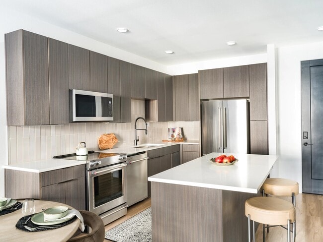 Contemporary kitchen design with rich-toned cabinetry, stainless steel appliances, and a spacious island perfect for cooking or casual dining. - Modera Kierland