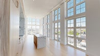 Located in Philadelphia's Northern Liberties neighborhood, this striking 2-bedroom, 3-bathroom residence showcases exceptional modern design throughout. The open-concept living and kitchen area is defined by dramatic double-height ceilings and expansive floor-to-ceiling gridded windows that flood the space with natural light and frame panoramic views of the Philadelphia skyline. Light-toned hardwood flooring runs seamlessly throughout, enhancing the bright, airy ambiance.

The gourmet kitchen is a standout, featuring a large waterfall-edge marble island, matching marble backsplash, warm wood cabinetry, a sleek cooktop with a stainless steel range hood, and double wall ovens. A light-filled hallway connects the main living areas to the private bedrooms, each offering generous proportions, soaring ceilings, and abundant natural light through large windows with city views. The primary bedroom is notably spacious and includes dedicated closet space.

The bathrooms are elegantly appointed with full-slab stone tile, frameless glass-enclosed showers, brushed gold fixtures, and floating white vanities. A private balcony with porcelain tile flooring and brick parapet walls offers sweeping, unobstructed views across Philadelphia's rooftops under open skies.