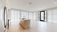 This well-appointed 2-bedroom, 2-bathroom residence offers a thoughtfully designed single-level layout with a clean, contemporary aesthetic throughout. The open-concept living area is anchored by a sleek kitchen featuring light wood cabinetry, stainless steel appliances, a central island with an integrated sink, and recessed lighting. Large floor-to-ceiling windows dressed with roller shades flood the space with natural light, while a black-framed glass door opens to a private balcony with outdoor views. Light wood-tone flooring flows seamlessly throughout, enhancing the bright and airy ambiance. The living room is generously sized and offers a flexible, open feel that connects naturally to the kitchen and dining area. The primary bedroom includes a ceiling fan, a private en-suite bathroom with a floating vanity, framed mirror, soaking tub, and tile surround, as well as access to a spacious walk-in closet with built-in shelving and hanging rods. The second bedroom is well-proportioned, featuring a ceiling fan and a wide window with blinds. Additional spaces include a den, a dedicated laundry area, multiple closets, and a hallway that ties the layout together efficiently.