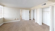 This single-floor residence offers a well-organized layout spread across multiple rooms, as revealed by the detailed floor plan. The living areas are generously proportioned, finished with warm neutral-toned carpet throughout and painted in soft beige tones that create a clean, understated ambiance. Large multi-pane windows fitted with horizontal blinds allow abundant natural light to flow through the main rooms, enhancing the sense of openness and space.

The bedroom areas are notably spacious, with one room featuring elegant crown molding and a row of large windows that flood the space with light. Closet space is plentiful, with bifold-door closets providing organized storage solutions. An additional bedroom includes a built-in closet and shares the same neutral carpet and light-toned walls.

The galley-style kitchen is efficiently designed, featuring white cabinetry on both sides, light wood-tone flooring, recessed ceiling lights, a double basin sink, a standard electric range, a refrigerator, and a dishwasher — offering full functionality in a compact, streamlined layout.

The bathroom is clean and simply appointed, with a full-size soaking tub and shower combination, a toilet, and wood-tone flooring. Throughout the unit, the consistent neutral palette and practical finishes contribute to a bright, move-in-ready living environment.
