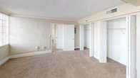 This single-floor residence offers a well-organized layout spread across multiple rooms, as revealed by the detailed floor plan. The living areas are generously proportioned, finished with warm neutral-toned carpet throughout and painted in soft beige tones that create a clean, understated ambiance. Large multi-pane windows fitted with horizontal blinds allow abundant natural light to flow through the main rooms, enhancing the sense of openness and space.

The bedroom areas are notably spacious, with one room featuring elegant crown molding and a row of large windows that flood the space with light. Closet space is plentiful, with bifold-door closets providing organized storage solutions. An additional bedroom includes a built-in closet and shares the same neutral carpet and light-toned walls.

The galley-style kitchen is efficiently designed, featuring white cabinetry on both sides, light wood-tone flooring, recessed ceiling lights, a double basin sink, a standard electric range, a refrigerator, and a dishwasher — offering full functionality in a compact, streamlined layout.

The bathroom is clean and simply appointed, with a full-size soaking tub and shower combination, a toilet, and wood-tone flooring. Throughout the unit, the consistent neutral palette and practical finishes contribute to a bright, move-in-ready living environment.