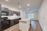 This single-floor, 1-bedroom, 1-bathroom residence offers a thoughtfully designed layout that maximizes its efficient footprint. The open-concept kitchen and living area serves as the heart of the home, featuring rich dark-stained cabinetry, granite countertops, and a prominent kitchen island that provides additional workspace and casual seating. Black appliances, including a refrigerator, range, and dishwasher, complement the kitchen's contemporary aesthetic. Recessed lighting and a ceiling fan keep the space bright and comfortable throughout.

The living area flows seamlessly from the kitchen, showcasing light hardwood-style flooring and a large window with blinds that invites natural light and outdoor views. The bedroom is a comfortable retreat, carpeted for warmth and equipped with its own ceiling fan and window overlooking the outdoors. A dedicated closet provides convenient storage adjacent to the bedroom.

The bathroom is clean and modern, featuring wood-look tile flooring, a granite-topped vanity with dark cabinetry, and a walk-in shower with a white tile surround. Neutral tones and crisp white walls throughout the entire residence create a bright, cohesive, and move-in-ready atmosphere.