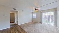 This single-floor residence offers a practical and functional layout across its well-defined living spaces. The main living area is generously sized, featuring plush wall-to-wall carpeting, a ceiling fan with light fixture, and dual access to the outdoors through a sliding glass door flanked by vertical blinds and an adjacent window, allowing natural light to fill the room. The transition to the dining area is marked by a shift to warm wood-look flooring, anchored by a classic pendant light overhead that adds a welcoming ambiance. The kitchen features a pass-through design with a raised bar-height counter, wood-toned cabinetry, a granite-style countertop, and black appliances, creating an efficient and connected cooking space. The bedrooms are carpeted and equipped with ceiling fans, offering comfortable, well-ventilated retreats. One bedroom is notably spacious, featuring three six-panel doors that lead to multiple closets, providing generous storage. The full bathroom is finished with wood-look flooring, a warm-toned vanity with an integrated sink, and a tiled shower-tub combination. Throughout the space, textured ceilings, neutral wall tones, and clean white trim contribute to a cohesive and understated aesthetic.