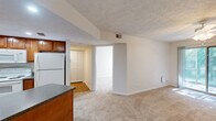 Located at 6650 Creek Bay Dr in Indianapolis, Indiana, this one-bedroom, one-bathroom residence offers a practical and comfortable single-floor layout. The open-concept living, dining, and kitchen area creates a connected, functional space ideal for everyday living. The kitchen is well-appointed with warm medium-toned wood cabinetry, dark granite-style countertops, a breakfast bar peninsula, and a full suite of white appliances including a range, over-the-range microwave, refrigerator, and dishwasher. Wood-look flooring grounds the kitchen, while plush carpet flows throughout the living and bedroom areas, adding warmth underfoot. The living room benefits from a ceiling fan and a pendant light over the dining area, providing both comfort and ambiance. A louvered closet door is visible near the kitchen transition, adding a classic touch. The bedroom offers a comfortable footprint with a window fitted with blinds for natural light and privacy, along with a dedicated closet. The unit also includes a utility room and a laundry area, adding everyday convenience. With three closets total throughout the home, storage is well-distributed. Textured ceilings and neutral walls provide a clean, move-in-ready canvas throughout.