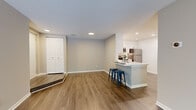 This single-floor, two-bedroom, one-bathroom residence in Reston, Virginia offers a thoughtfully designed open-concept layout. The combined living and kitchen area serves as the heart of the home, featuring wood-style plank flooring throughout and recessed lighting overhead. The kitchen is outfitted with white shaker-style cabinetry, white quartz countertops, a subway tile backsplash, and a full suite of stainless steel appliances including a refrigerator, range, microwave, and dishwasher. A peninsula with a built-in sink and seating for two extends into the living area, enhancing functionality. The living room receives natural light through a sliding glass door that opens onto a private balcony with outdoor views of surrounding trees. Both bedrooms are carpeted and feature neutral walls, windows with blinds admitting natural light, and a spacious, versatile layout. A closet with bi-fold doors provides additional storage. The bathroom is clean and bright, finished with white cabinetry, a white countertop vanity, a medicine cabinet mirror, and wood-style flooring consistent with the rest of the home.