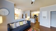 Located at 4130 Garrett Rd in Durham, North Carolina, this single-floor residence offers a thoughtfully designed open-concept layout that maximizes both functionality and comfort. The living area serves as the heart of the home, featuring rich hardwood flooring, a ceiling fan, and track lighting that provides ample illumination throughout the space. Crown molding along the walls adds a refined architectural touch. The living room flows naturally into the kitchen, which is defined by a raised bar-height peninsula that doubles as a casual dining and prep space. The kitchen is equipped with black appliances, warm honey-toned cabinetry, and additional track lighting overhead, creating a bright and efficient workspace. A large mirror in the living area reflects light and enhances the sense of openness. The neutral color palette of soft whites and warm grays throughout the space lends a clean, modern aesthetic that is both welcoming and versatile. The open sightlines between rooms make the interior feel expansive and airy, ideal for everyday living and entertaining alike. The overall ambiance is contemporary and comfortable, with practical details that elevate the day-to-day living experience.