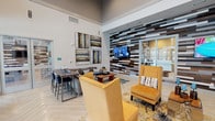 Located at 1626 N Ellison Dr in San Antonio, Texas, the Estraya Hills community clubhouse is a thoughtfully designed single-floor amenity space that blends modern aesthetics with inviting comfort. The main lounge area features soaring ceilings, herringbone-patterned light wood flooring, and a bold accent wall constructed from mixed wood planks in varying tones, creating a striking visual centerpiece. A wall-mounted flat-screen television anchors this area, complemented by plush gold accent chairs, a sectional sofa, and a dining-height table with bar seating — ideal for both casual gatherings and social events. A floor-to-ceiling stone fireplace anchors a cozy seating nook, adding warmth and a classic architectural touch. The game room is a standout feature, equipped with a regulation pool table and flooded with natural light through full-height glass garage doors that open directly to an outdoor terrace, seamlessly connecting the interior to the exterior. A separate lounge area is finished in calming teal tones, adorned with a vibrant sculptural wall installation and furnished with light-colored seating and bar-height tables. Throughout the space, recessed lighting and curated artwork contribute to an upscale, welcoming ambiance suited for community living.
