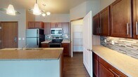 Located on Calico Drive South in Fargo, North Dakota, this single-floor residence offers a well-designed layout with quality finishes throughout. The kitchen is a standout feature, showcasing rich cherry-toned cabinetry, granite-style countertops, a subway tile backsplash, and a full suite of stainless steel appliances including a refrigerator, electric range, and built-in microwave. A central island with a built-in sink and pendant lighting adds both style and functionality, while a walk-in pantry provides generous storage. The kitchen flows naturally into a dedicated dining or workspace area and connects to the main living room. The living area is generously sized, featuring recessed lighting, large windows that invite natural light, and a combination of durable wood-style flooring and plush carpeting. Bedrooms are carpeted and well-proportioned with ample wall space. A built-in desk nook adds a practical workspace element. Two bathrooms are finished with granite-topped cherry vanities and tile flooring; one includes a tub/shower combo. A dedicated in-unit laundry room is equipped with a full-size front-loading washer and dryer alongside wire shelving for added storage convenience.