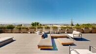 Located at 1700 Newbury Park Drive in San Jose, California, this thoughtfully designed rooftop deck offers an expansive outdoor retreat with a distinctly modern aesthetic. The space is finished with wide-plank composite decking in a cool gray tone, providing a clean and contemporary foundation throughout.

Multiple seating zones are arranged across the deck to accommodate a variety of uses. One area features low-profile teak-framed sofas and chaise lounges with plush gray cushions, centered around a slatted wood coffee table — ideal for relaxed conversation or lounging. A second zone is appointed with crisp white-cushioned teak armchairs and a round pedestal side table, offering a more intimate setting. A dedicated sun terrace is lined with a row of padded chaise loungers, perfectly oriented for enjoying abundant California sunshine.

Generously sized concrete and neutral-toned planters are arranged along the perimeter and throughout the space, filled with a vibrant mix of palms, ornamental grasses, red flowering shrubs, and tropical foliage that adds color and a sense of privacy. The open-sky exposure ensures exceptional natural light throughout the day. Sweeping views of the surrounding San Jose skyline and distant mountains complete the experience, making this rooftop deck a compelling outdoor amenity suited for both social gatherings and quiet relaxation.