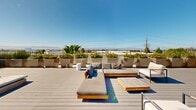 Located at 1700 Newbury Park Drive in San Jose, California, this thoughtfully designed rooftop deck offers an expansive outdoor retreat with a distinctly modern aesthetic. The space is finished with wide-plank composite decking in a cool gray tone, providing a clean and contemporary foundation throughout.

Multiple seating zones are arranged across the deck to accommodate a variety of uses. One area features low-profile teak-framed sofas and chaise lounges with plush gray cushions, centered around a slatted wood coffee table — ideal for relaxed conversation or lounging. A second zone is appointed with crisp white-cushioned teak armchairs and a round pedestal side table, offering a more intimate setting. A dedicated sun terrace is lined with a row of padded chaise loungers, perfectly oriented for enjoying abundant California sunshine.

Generously sized concrete and neutral-toned planters are arranged along the perimeter and throughout the space, filled with a vibrant mix of palms, ornamental grasses, red flowering shrubs, and tropical foliage that adds color and a sense of privacy. The open-sky exposure ensures exceptional natural light throughout the day. Sweeping views of the surrounding San Jose skyline and distant mountains complete the experience, making this rooftop deck a compelling outdoor amenity suited for both social gatherings and quiet relaxation.