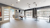 This thoughtfully designed single-floor amenity space offers a generous and versatile layout spanning a substantial footprint. The space is organized into distinct functional zones connected by a central hallway, each reflecting a cohesive modern aesthetic.

The kitchen and living room area serves as a social hub, featuring a U-shaped kitchen outfitted with dark granite countertops, gray shiplap backsplash, stainless steel appliances, and large-format tile flooring. Adjacent lounge areas display a striking teal-painted ceiling, exposed brick accent walls, and colorful artwork, creating a vibrant atmosphere. Comfortable seating arrangements and high-top tables make this zone ideal for gathering and relaxation.

A game and social room showcases industrial-style overhead garage doors that flood the space with natural light and views of the surrounding greenery. Light tile flooring, a shuffleboard table, wall-mounted television, and bar-height seating round out this lively entertainment area.

The dedicated exercise room is well-appointed with treadmills, ellipticals, free weights, and organized equipment storage. A bold teal ceiling, exposed brick columns, large windows, and ceiling fans contribute to an energizing workout environment. Carpeted flooring and ample natural light enhance the space's functionality and comfort throughout.