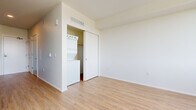 This single-floor studio is a well-organized and modern living space that makes efficient use of its compact footprint. The layout follows a straight, open corridor design that connects the entry and kitchen to the living area, creating a natural flow throughout.

The galley-style kitchen is a standout feature, outfitted with dark flat-panel cabinetry, black granite-style countertops, and a suite of stainless steel appliances including a refrigerator, electric range, built-in microwave, and dishwasher. A textured charcoal backsplash adds a contemporary visual contrast to the clean lines of the cabinetry.

Light-toned hardwood-style flooring runs throughout the entire space, lending warmth and visual continuity. The living area is bright and open, with white walls and a large window that invites natural light and provides outdoor views of the surrounding neighborhood. The airy, minimalist aesthetic makes the space feel larger than its footprint suggests.

A dedicated closet area in the living space houses a stacked in-unit washer and dryer — a highly practical feature. Additional storage is available through a sliding-door closet. The clean, neutral palette of white walls and light flooring throughout creates a calm and versatile ambiance, ready to accommodate a variety of furniture arrangements and personal styles.