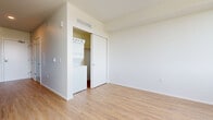 This single-floor studio is a well-organized and modern living space that makes efficient use of its compact footprint. The layout follows a straight, open corridor design that connects the entry and kitchen to the living area, creating a natural flow throughout.

The galley-style kitchen is a standout feature, outfitted with dark flat-panel cabinetry, black granite-style countertops, and a suite of stainless steel appliances including a refrigerator, electric range, built-in microwave, and dishwasher. A textured charcoal backsplash adds a contemporary visual contrast to the clean lines of the cabinetry.

Light-toned hardwood-style flooring runs throughout the entire space, lending warmth and visual continuity. The living area is bright and open, with white walls and a large window that invites natural light and provides outdoor views of the surrounding neighborhood. The airy, minimalist aesthetic makes the space feel larger than its footprint suggests.

A dedicated closet area in the living space houses a stacked in-unit washer and dryer — a highly practical feature. Additional storage is available through a sliding-door closet. The clean, neutral palette of white walls and light flooring throughout creates a calm and versatile ambiance, ready to accommodate a variety of furniture arrangements and personal styles.
