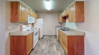 This single-floor residence offers a thoughtfully designed layout that balances functionality and comfort throughout. The galley-style kitchen is well-equipped with warm honey-toned wood cabinetry lining both walls, ample counter space, and a full suite of white appliances including a refrigerator, electric range with overhead microwave, and dishwasher, all set atop wood-look flooring that adds a clean, modern touch.

The living area is carpeted and spacious, featuring a ceiling fan with light fixture and a sliding glass door framed by vertical blinds that invites natural light into the room. Multiple bedrooms continue the carpeted flooring and are filled with natural light through sizable windows fitted with blinds. One bedroom includes a generous walk-in closet outfitted with a full wire shelving and hanging rod system, providing excellent storage organization.

Both bathrooms are appointed with wood-look tile flooring, warm-toned vanities with countertop sinks, and full tub-shower combinations. A dedicated laundry area features a side-by-side washer and dryer tucked behind double bi-fold doors, accented by a chandelier overhead. The overall aesthetic is neutral and bright, with consistent finishes creating a cohesive, move-in-ready environment throughout.