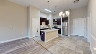 Located at 920 Seasons Dr in Gastonia, North Carolina, this single-floor residence offers a thoughtfully designed layout with modern finishes throughout. The open-concept kitchen is a standout feature, showcasing rich dark cabinetry, granite countertops, stainless steel appliances, and a central island illuminated by pendant lighting. Soaring ceilings with a skylight allow natural light to flood the space, creating a bright and airy atmosphere. The kitchen flows seamlessly into the dining and living areas, where wood-look flooring and neutral warm-toned walls provide a cohesive, welcoming aesthetic. The spacious living area is highlighted by a ceiling fan and a set of French doors that open to an outdoor view, allowing ample natural light to enter. A secondary room also features French doors and a pendant light fixture, with direct access to a walk-in closet. The walk-in closet is generously sized with wire shelving on both sides and connects directly to the bathroom. The bathroom is elegantly finished with large-format stone-look tile, a dual-sink vanity with granite countertops and dark cabinetry, a walk-in shower with floor-to-ceiling tile surround, and a large mirror. Throughout the residence, consistent wood-look and tile flooring, crisp white trim, and neutral walls create a clean, modern, and move-in ready environment.