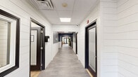 Located at 800 Cassata Dr in Copiague, NY, this single-floor facility offers a thoughtfully designed layout that balances comfort, recreation, and fitness. The welcoming reception lounge features light wood-style flooring, a drop ceiling with flush panel lighting, clean white walls, and contemporary furnishings including a sage green sofa, cognac leather accent chairs, and an organic-shaped coffee table. Large double glass doors flood the space with natural light, while curated artwork and greenery add warmth to the atmosphere. A dedicated exercise room is outfitted with a dark drop ceiling and an impressive array of equipment, including strength machines, stationary bikes, a treadmill, and stability balls, all set on durable wood-style flooring with natural light filtering through shaded windows. A separate game room provides a relaxed setting centered around a full-size billiard table, brightened by multiple windows with woven shades and accented with botanical décor. A dining and lounge area features a bold blue shiplap accent wall, built-in booth seating, and bistro-style tables, creating an inviting social space. Six connecting hallways ensure smooth flow throughout the facility, while a clean, fully tiled bathroom with modern fixtures rounds out the practical amenities of this versatile community-oriented space.