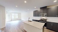 This well-appointed one-bedroom, one-bathroom residence in Skillman, NJ offers a thoughtfully designed single-floor layout that maximizes every square foot. The open-concept kitchen and living area serves as the heart of the unit, anchored by a striking granite-topped island with an undermount sink. Dark shaker-style cabinetry reaches toward the ceiling, providing ample storage, while stainless steel appliances—including a gas range, built-in microwave, and French door refrigerator—add a polished, modern touch. A white subway tile backsplash and warm wood-tone flooring complement the contemporary aesthetic throughout.

The living area is bright and airy, with recessed lighting and a window that invites natural light. The bedroom features soft carpeting and a neutral palette, creating a calm retreat. The bathroom includes a tiled tub-shower combination with a decorative mosaic accent border and a dark-cabinet vanity. A dedicated laundry area houses a stacked washer and dryer for added convenience. The building exterior features a multi-story facade with stone accents and access to a beautifully landscaped courtyard with paved seating areas and mature trees.