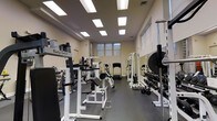 Located at 224 1st Ave in Columbus, Ohio, this fitness facility offers a thoughtfully organized workout space designed to accommodate a range of exercise needs. The single-floor layout is arranged to maximize usable floor space, with equipment positioned along the perimeter and throughout the center of the room, allowing for efficient traffic flow during workouts.

The space features a notable selection of strength training equipment, including Body-Solid machines, cable systems, weight racks stocked with dumbbells and plate weights, and multi-function press stations. Cardio equipment, including a treadmill and stationary bike, is positioned toward the back of the room near a window that allows natural light to filter in.

The interior is finished with light-colored walls and a dark rubber flooring, which provides both durability and safety underfoot. Overhead, recessed panel lighting is evenly distributed across the ceiling, ensuring consistent illumination throughout the entire space. The overall ambiance is clean, functional, and purposeful, reflecting a no-frills approach oriented toward serious fitness use. The layout and equipment selection make this facility suitable for both individual training and structured workout programming.