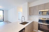 Located at 4465 Griffin Rd in Hollywood, FL, this well-appointed 2-bedroom, 2-bathroom residence offers a thoughtfully designed single-floor layout with a clean, contemporary aesthetic. Light wood-tone flooring runs throughout the living areas and bedrooms, complementing the bright white walls and modern black hardware accents.

The open-concept living and dining area flows naturally from the kitchen, which features warm wood cabinetry, quartz countertops, a marble-style tile backsplash, stainless steel appliances including a French door refrigerator, and a peninsula with an undermount sink and professional-style faucet. Floor-to-ceiling sliding glass doors lead to a private balcony, flooding the living space with natural light and offering views of the surrounding area.

Both bedrooms are well-proportioned and bright, with the primary bedroom featuring its own sliding glass door access to the balcony. The two bathrooms are finished with neutral tile flooring, wood-tone vanities, white quartz countertops, and marble-tiled showers. Storage is generously provided through five closets, including a walk-in closet with wire shelving. A dedicated laundry area and two hallways round out the functional layout of this modern Hollywood residence.